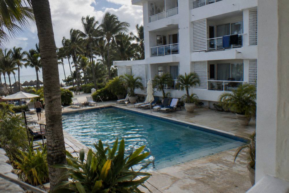 Low-rise four-storey hotel with white balconies above a small courtyard pool and palms